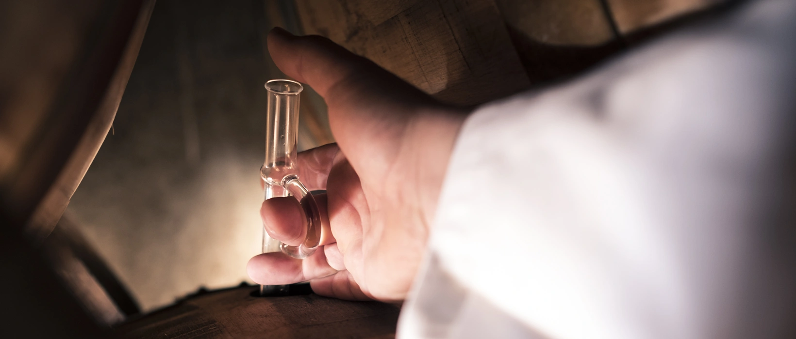Brennmeister entnimmt mit einem gläsernen Stechheber eine Grappa-Probe aus dem Barrique in der Brennerei Castagner